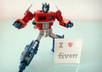 take 3 pictures of Optimus Prime doing a cool pose while holding a sign or message